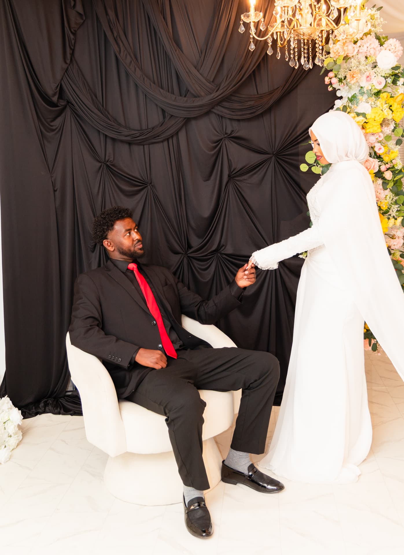 Couple posing against a black draped studio backdrop with floral arch