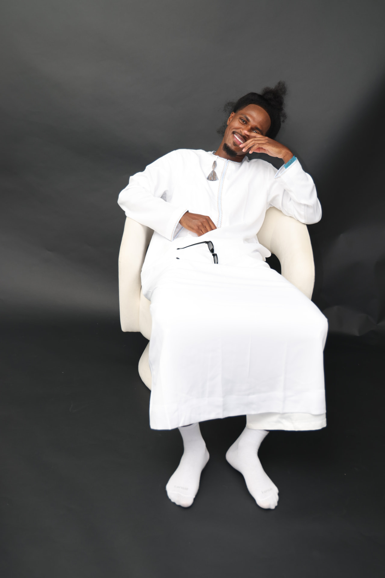 Man in white traditional attire relaxed on a cream chair in the Xirfad Studio
