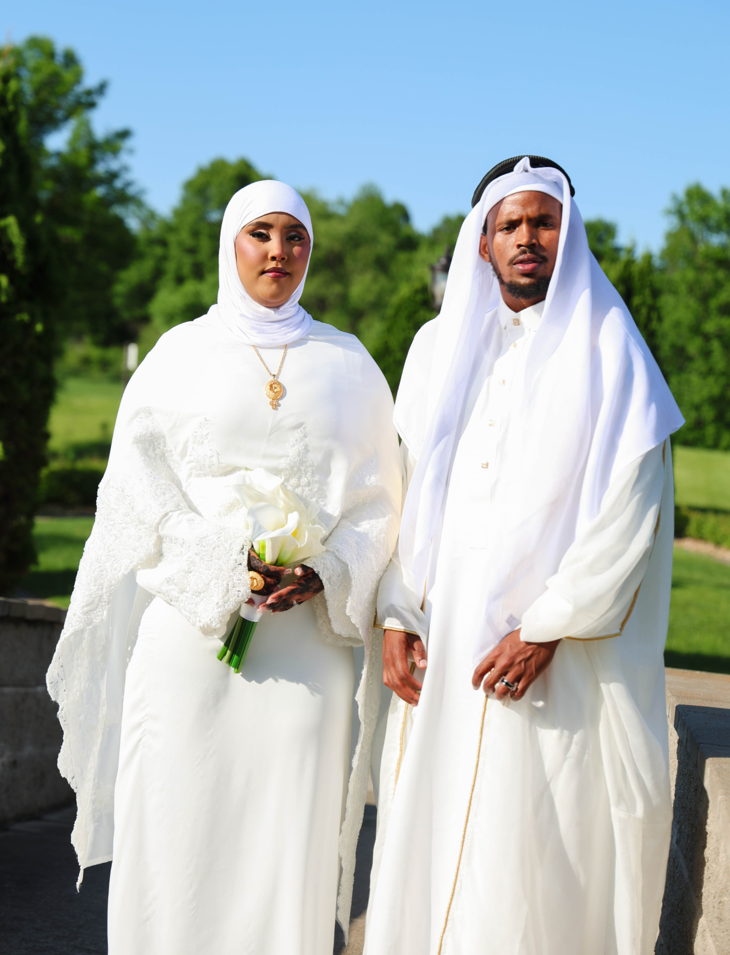 Bride and groom in white attire with calla lily bouquet outdoors