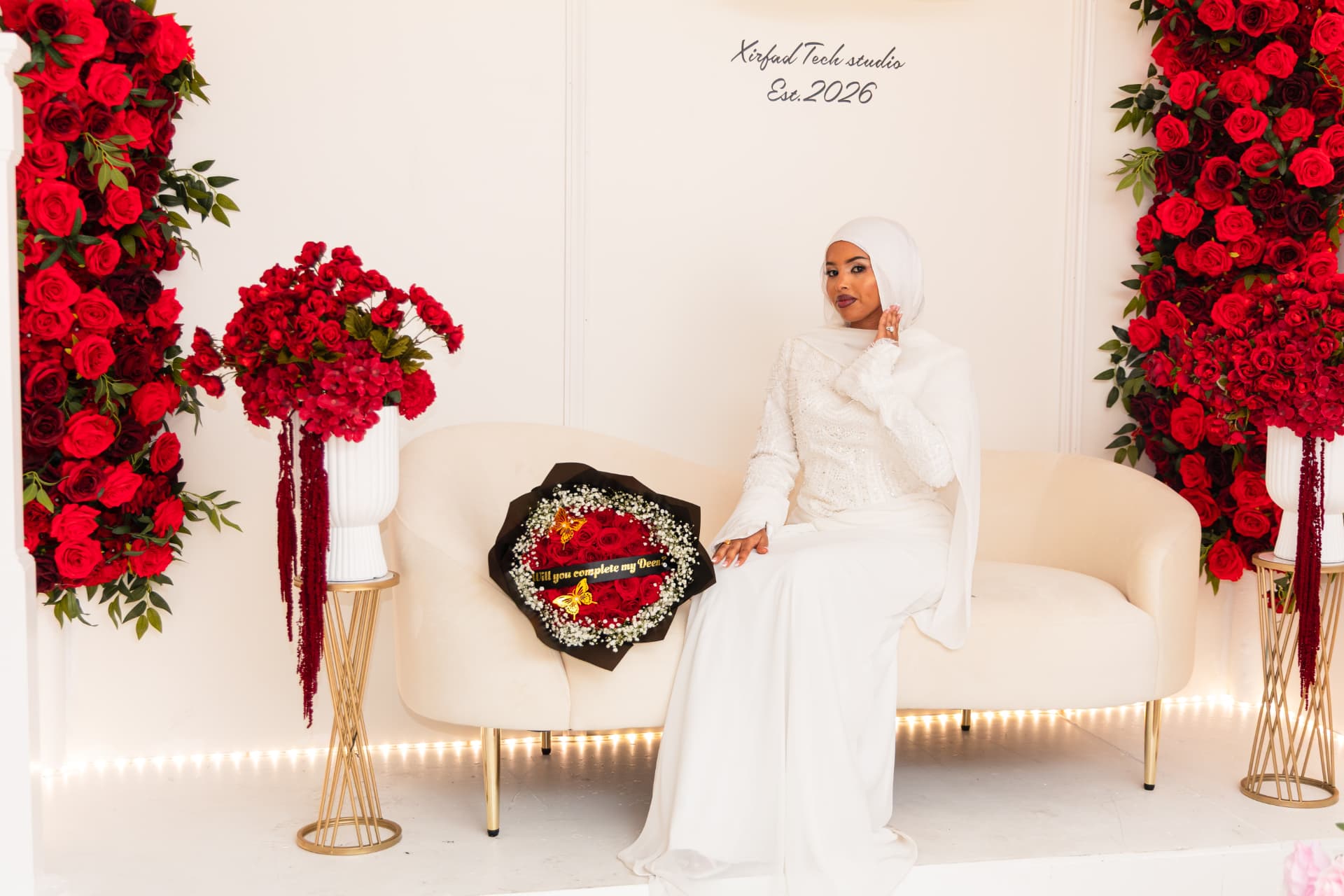 Bride seated on cream sofa in the Xirfad Studio red rose backdrop