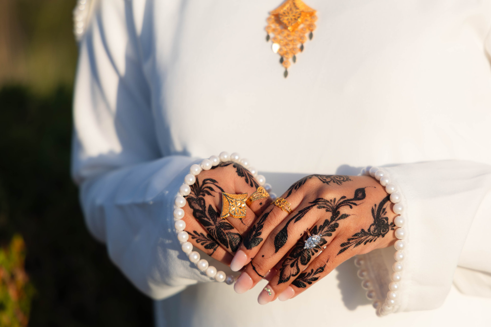 Bride's henna-covered hands with gold rings and pearl cuffs in warm sunlight