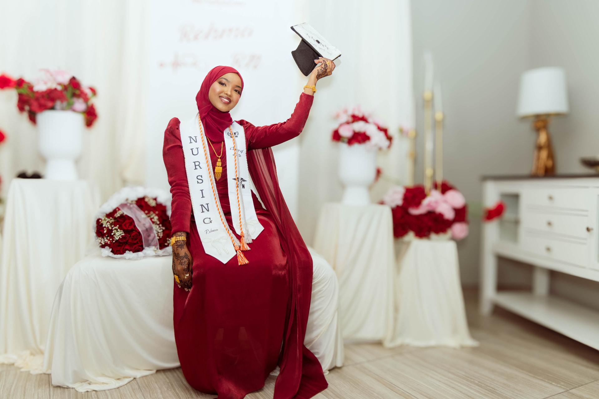 Nursing graduate in crimson holding her decorated cap in the Xirfad Studio rose setup