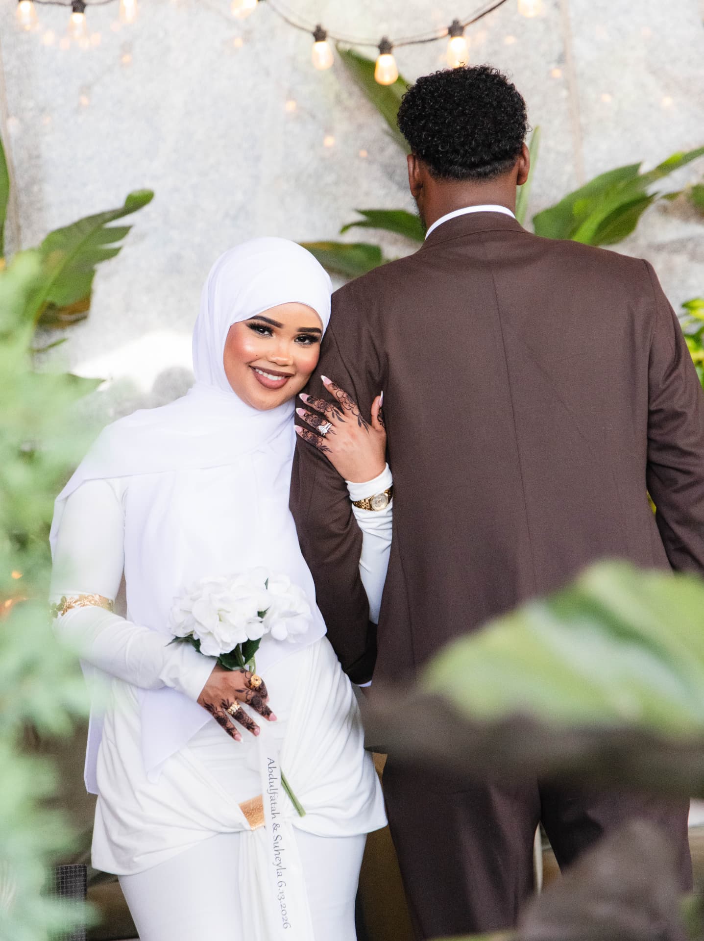 Bride in white smiling beside her groom under warm string lights in a garden setting