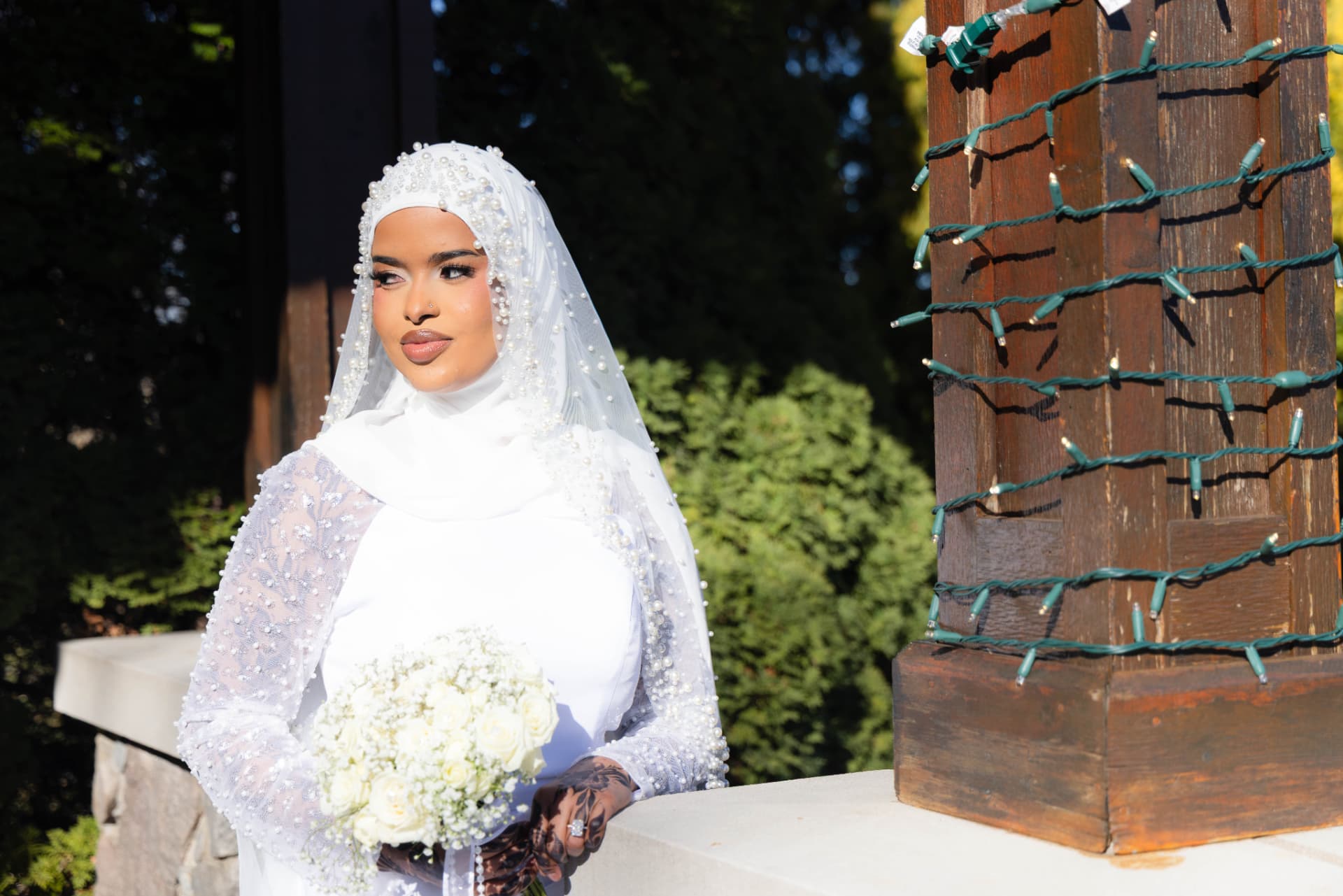 Bride in a pearl veil holding white roses in golden sunlight