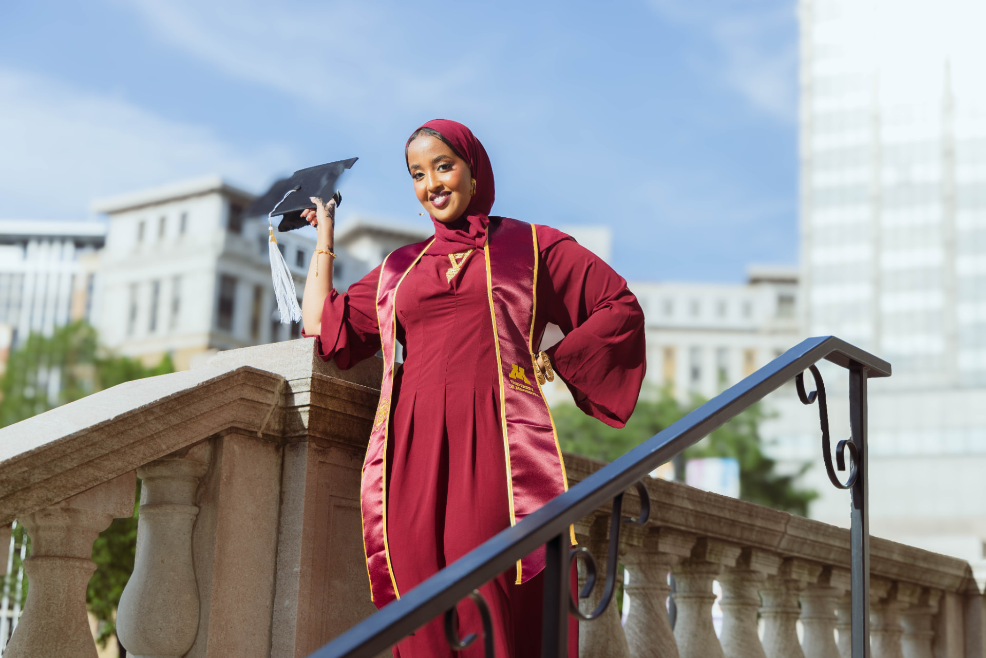 Graduate in maroon University of Minnesota regalia holding her cap