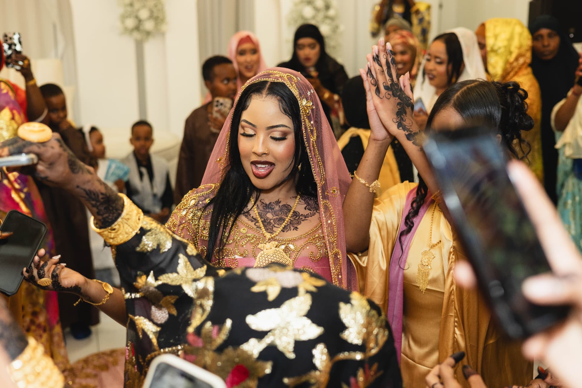 Bride celebrating with guests in gold jewelry and henna at a Somali wedding
